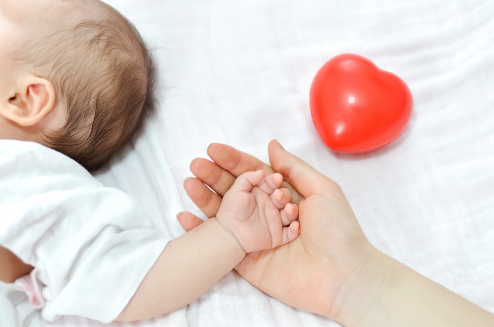 caregiver holding sleeping infant’s hand to monitor comfort and breathing